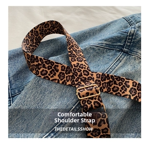 Close-up of leopard print fabric strap with gold metal buckle on denim background