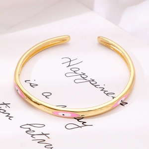 Dettaglio del bracciale rigido dorato con occhio del male in smalto rosa e bianco