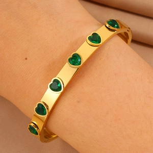 Détail d'un bracelet en acier titane plaqué or orné de zircons en forme de cœur vert