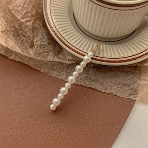 Close-up of golden hair clip featuring gradient white pearls on brown leather backdrop