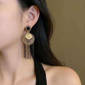 Boucles d'oreilles vintage dorées avec pièce portrait et franges noires sur modèle