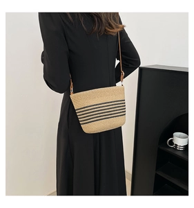 Detail of a striped straw crossbody bag with brown strap shown on a model