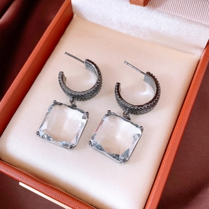 Macro detail of square crystal earrings with dark metal engraved textures on silk lining