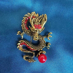 Detailansicht einer goldenen Drachenbrosche mit roten Strasssteinen und einer Perle