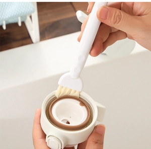 Close-up of dual-head cleaning brush scrubbing a bottle lid seal in a bright kitchen