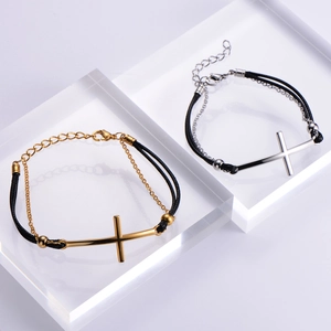 Gros plan des bracelets croix or et argent avec cordons en cuir noir sur blocs acryliques