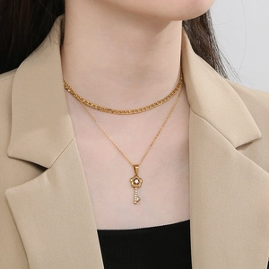Detail view of a double-layer gold necklace featuring a floral key pendant with small diamonds