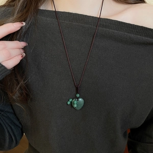 Detail of a green heart stone pendant on a brown woven rope necklace worn by a model