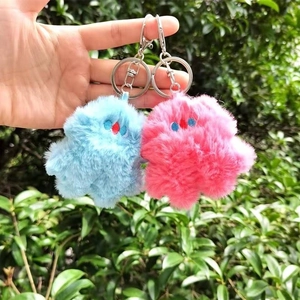 Close-up of blue and pink plush monster keychains held by hand outdoors