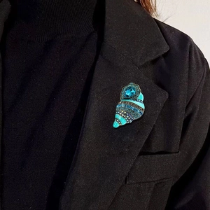 Vintage conch brooch with turquoise enamel and blue crystals on a black suit lapel