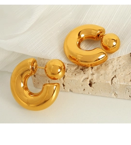 Detailed view of polished golden C-shaped hoop earrings with large spherical backing on fabric