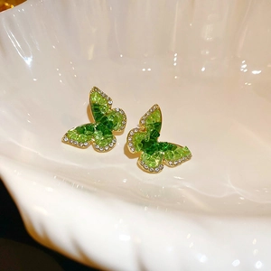 Macro shot of green crystal butterfly earrings with white rhinestones on golden base