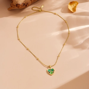 Detailed close-up of golden heart pendant featuring green gemstones on a beaded chain