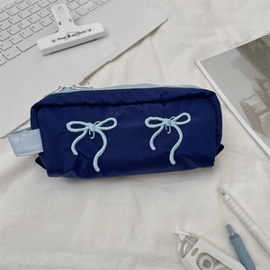 Large capacity navy pencil case with blue bow embroidery shown in a study desk setting