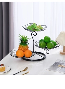 Detail of a 3-tier black metal leaf-shaped fruit basket on a modern white dining table