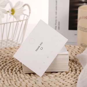 Close-up of white Thank You jewelry display cards with earring holes on a woven mat