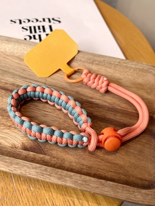 Macro detail of braided phone wrist strap in orange and grey with adjustment buckle