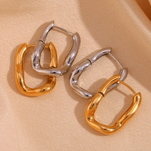 Macro shot of irregular U-shaped geometric earrings in gold and silver finish on silk