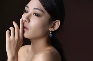 Luxurious dangling aquamarine earrings with halo diamonds on a model's ear