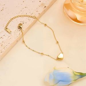 Detail of a golden heart pendant and bead chain on a textured stone surface with flowers