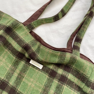 Detail of green and brown checkered tote bag with woven label and suede handles