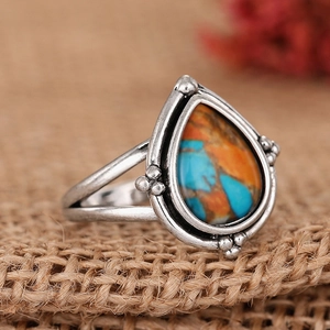 Détail macro d'une bague argentée vintage avec pierre goutte orange et turquoise