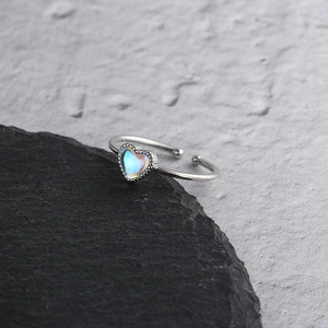 Macro shot of silver heart ring with moonstone gemstone on textured black stone