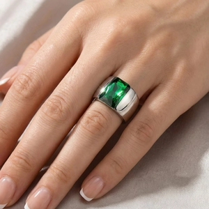 Detail of a minimalist wide silver ring featuring a large emerald-cut green gemstone