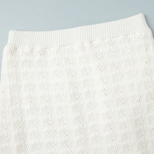 Close-up of white knitted skirt featuring elastic ribbed waist and hollow geometric patterns