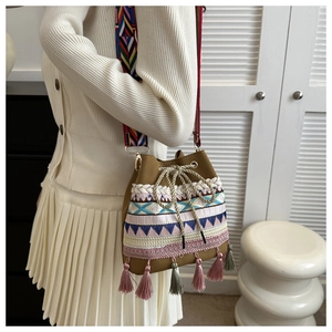 Detail of bohemian bucket bag featuring colorful embroidery, tassels and a woven strap
