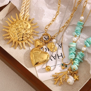18K gold plated necklace with coral, heart locket, shell charms and sun pendant on tray