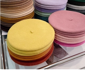 Close-up of stacked thick wool beret hats in vibrant yellow, pink, purple and brown colors