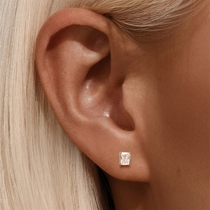 Close-up of a square-cut zircon stud earring with gold plating worn on an earlobe