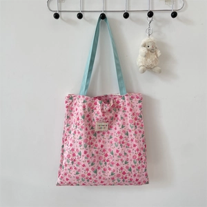 Detail of floral tote bag with light blue handles and a decorative woven brand label