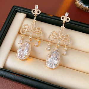Détail macro de boucles d'oreilles goutte dorées avec zircone sur velours beige