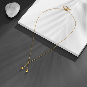 Detailed view of gold double ball pendant necklace on elegant stone display with palm shadows