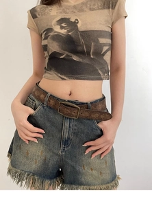 Close-up of a vintage brown embossed leather belt paired with distressed denim shorts
