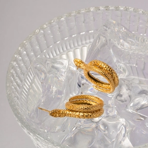 Detailed close-up of gold snake earrings resting on ice in a crystal glass bowl