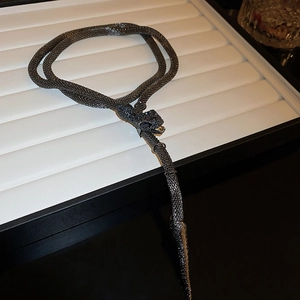Detailed close-up of a dark metal snake necklace with intricate mesh scales and blue gemstone eyes