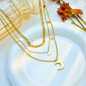 Three-layer gold star and moon pendant necklace displayed on a white plate with dry flowers