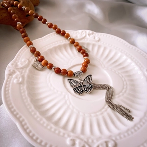 Détail d'un collier vintage en ébène avec pendentif papillon argenté et pompon sur soie