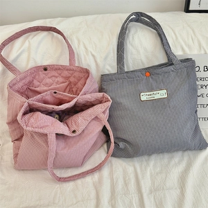 Detail of quilted plaid tote bags in red and blue with metal snap button and logo patch