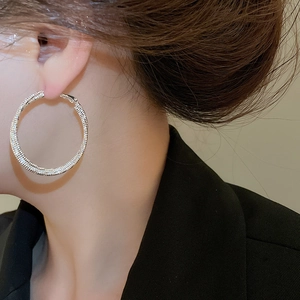 Close-up of a silver-colored large round metal earring with textured glitter finish on a model