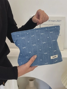 Denim toiletry bag with white bow pattern and brand label held in hands