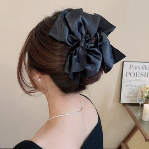 Detail of a large black satin bow hair claw clip worn by a model in a French chic style