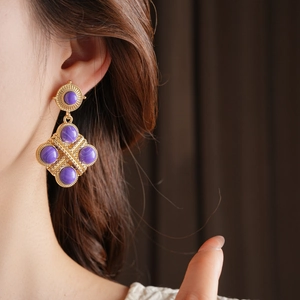 Dettaglio di orecchini vintage dorati con gemme viola e pendente a forma di rombo