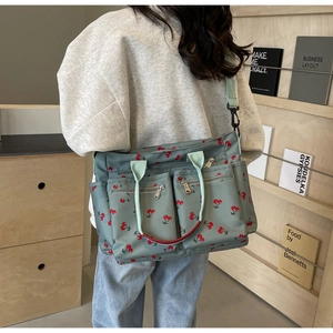 Lifestyle shot of large grey-green canvas tote bag with red cherry print on a wooden shelf