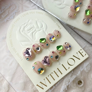 Detail of luxury press-on nails with colorful heart and emerald gems on rose card