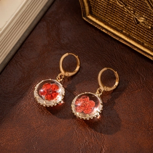Detail of vintage gold earrings featuring red dried flowers in transparent glass spheres