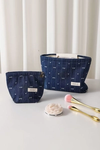 Detail of denim cosmetic bags with white bow embroidery and petal-shaped metal zippers